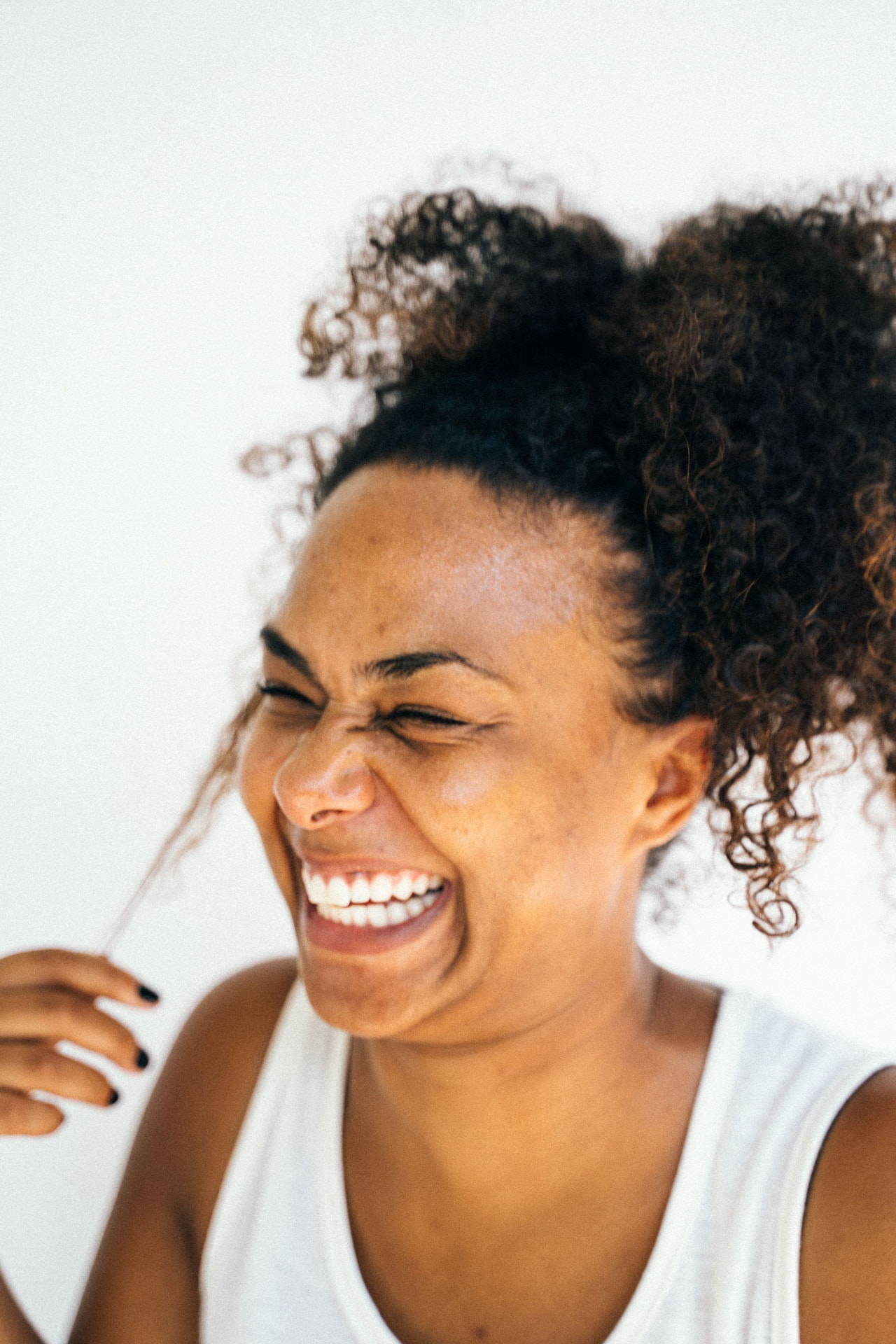 A woman laughing freely with curly hair against a soft white background